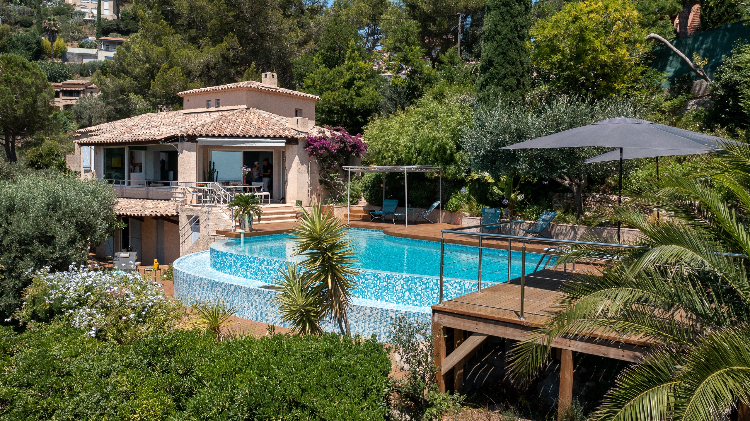 Villa provençale avec piscine à débordement à plusieurs niveaux, terrasse en bois et jardin méditerranéen ensoleillé.