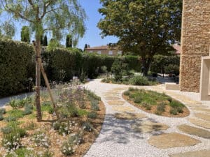 Jardin méditerranéen aménagé avec allée en gravier blanc, pas japonais en pierre naturelle et fleurs violettes.